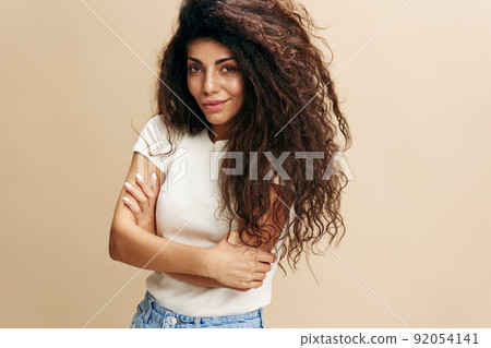 Gorgeous confident curly Latin female look at camera, crossing hands on the chest. Copy space for clothing fashion brands, free place for your ad. Studio shoot isolated over pastel beige background Gorgeous confident curly Latin female look at camera, crossing hands on the chest. Copy space for clothing fashion brands, free place for your ad. Studio shoot isolated over pastel beige background 92054141