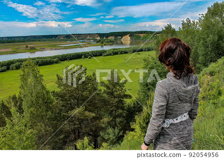 A girl standing on a hill, on a steep bank of a river in summer and looking into far away. A girl standing on a hill, on a steep bank of a river in summer and looking into far away. 92054956