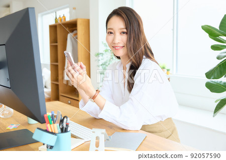 一個女人看著她的智能手機在她的辦公桌 92057590