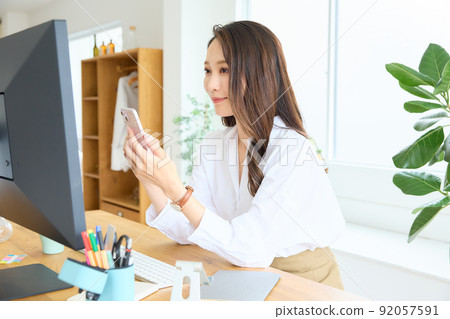 一個女人看著她的智能手機在她的辦公桌 92057591