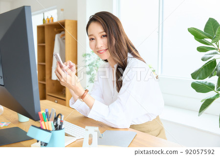 一個女人看著她的智能手機在她的辦公桌 92057592