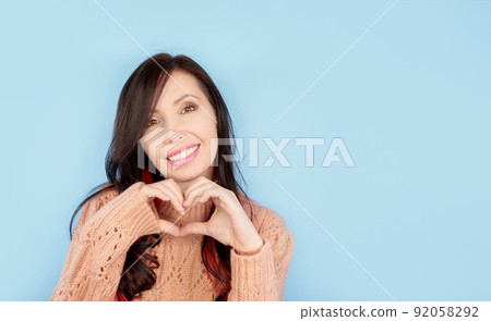 Smiling young american girl in casual coral knitted clothes showing shape heart with hands isolated on pastel blue background. People lifestyle concept. Mock up copy space. Heart-shape sign. 92058292