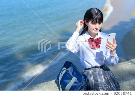高中女生應用 SNS 海邊沙灘 instagram,坐落在美麗的海邊防波堤上,使用智能手機 高中女生應用 SNS 海邊沙灘 instagram,坐落在美麗的海邊防波堤上,使用智能手機 92058741