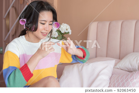 Portrait of asian woman rolling her hair and brushing her nails in pink bedroom Portrait of asian woman rolling her hair and brushing her nails in pink bedroom 92063450