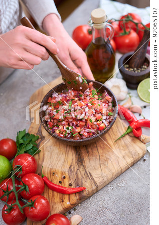 making salsa dip sauce - woman mixing chopped ingredients in wooden bowl making salsa dip sauce - woman mixing chopped ingredients in wooden bowl 92065102