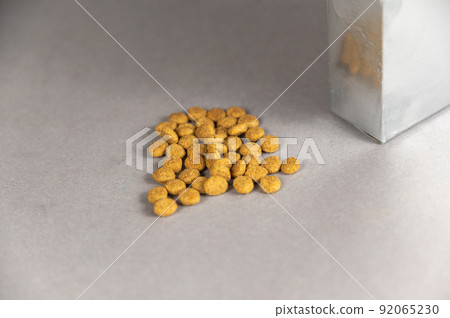 A silver rectangular box against a gray background. Pet food spilling out of the hole. Dry pelleted food. Pet food. Selective focus. A silver rectangular box against a gray background. Pet food spilling out of the hole. Dry pelleted food. Pet food. Selective focus. 92065230