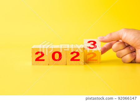 Hand flips wooden cubes with 2022 to 2023 on yellow background. 92066147