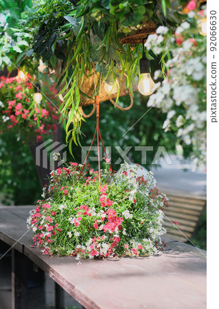 summer street cafe decor, romantic flowers and lamps over the wooden table. vertical shot of hanging flower basket. city decor, seasonal outdoor restaurant. summer street cafe decor, romantic flowers and lamps over the wooden table. vertical shot of hanging flower basket. city decor, seasonal outdoor restaurant. 92066630