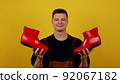 A gardener in overalls holds bright red boots in his hands. The concept of the beginning of the gardening season 92067182