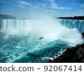 Niagara Falls. A cruise ship surrounded by fog in a basin. A large amount of water falling from a waterfall that spreads across the width. 92067414