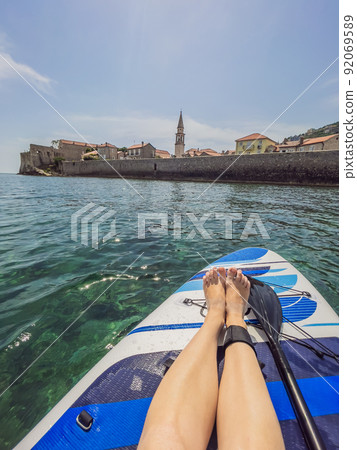 Summer holidays vacation travel. SUP Stand up paddle board. Young woman sailing on beautiful calm lagoon along Budva old town 92069589