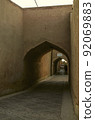 A narrow street with adobe houses in the old city of Yazd, which barely fit people and a car 92069883