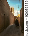 Street with adobe houses in the old city of Yazd with a view of the ventilation tower against the blue sky. 92069889