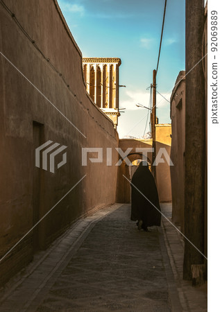 Street with adobe houses in the old city of Yazd with a view of the ventilation tower against the blue sky. Street with adobe houses in the old city of Yazd with a view of the ventilation tower against the blue sky. 92069889
