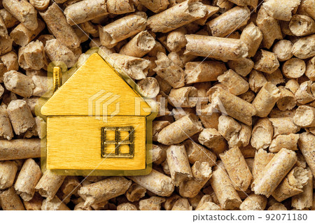 Small yellow house against wooden pellets background macro. Compacted sawdus as organic biofuel. Small yellow house against wooden pellets background macro. Compacted sawdus as organic biofuel. 92071180