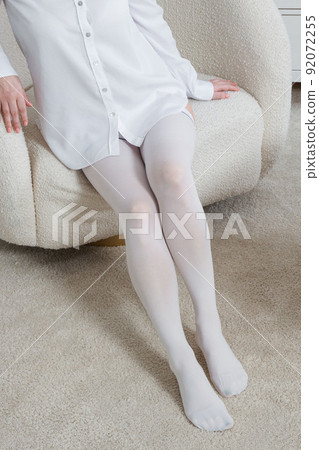 White hosiery. Beautiful long female legs in stockings. Girl putting on stockings at home in a white room. Varicose veins prevention. Woman body in underwear. White hosiery. Beautiful long female legs in stockings. Girl putting on stockings at home in a white room. Varicose veins prevention. Woman body in underwear. 92072255