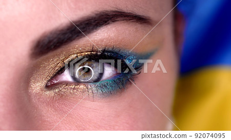 Macro view of woman eye with blue yellow shiny make-up. Lady, green cornea with round reflection Macro view of woman eye with blue yellow shiny make-up. Lady, green cornea with round reflection 92074095