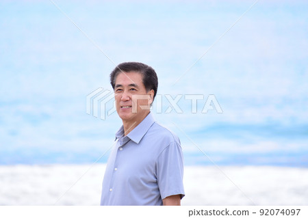 A refreshing senior man standing with a smile against the blue sea 92074097