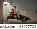 Woman wrapped herself in a blanket is drinking hot tea for colds. 92077735