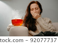 Woman coughs in hand with sore throat holding hot medicinal tea. 92077737