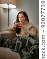 Woman at home is treated with hot tea while sitting on a beige sofa. 92077739