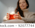 Woman warms her hands on a glass mug with tea on winter evening home. 92077744