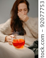 A mug of hot tea for colds and flu keeps the woman sick. 92077753