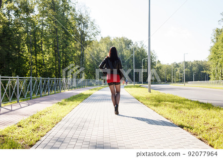 young brunette woman in red dress walking along the alley 92077964