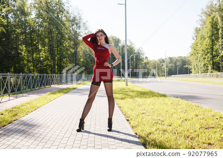 young brunette woman in red dress walking along the alley 92077965