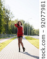 young brunette woman in red dress walking along the alley 92077981
