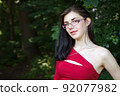 young brunette woman in a red dress and glasses in city park 92077982