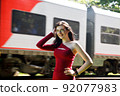 young brunette woman in red dress and glasses standing near railway 92077983