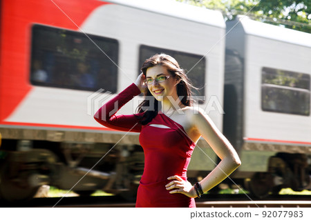 young brunette woman in red dress and glasses standing near railway 92077983