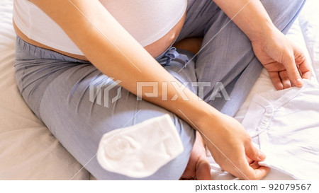 Pregnant woman baby clothes. Beautiful pregnancy mother with yellow baby clothes. Pregnant woman hugging belly and packing maternity hospital bag. Concept maternity, pregnancy, childbirth. Pregnant woman baby clothes. Beautiful pregnancy mother with yellow baby clothes. Pregnant woman hugging belly and packing maternity hospital bag. Concept maternity, pregnancy, childbirth. 92079567