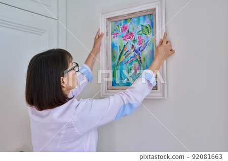 Woman hanging floral birds art framed at home on the wall Woman hanging floral birds art framed at home on the wall 92081663