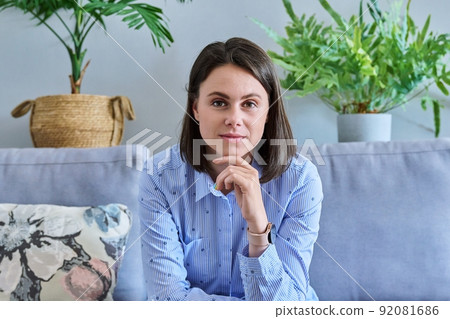 Young beautiful woman looking at camera while sitting on couch at home Young beautiful woman looking at camera while sitting on couch at home 92081686