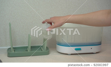 A woman removes children's dishes from a steam sterilizer and hangs them on a dryer. The sterilizer cleans germs and bacteria. 92081997