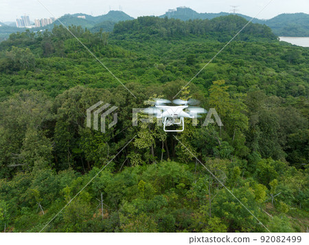 Flying white drone taking photo of landscape in forest Flying white drone taking photo of landscape in forest 92082499