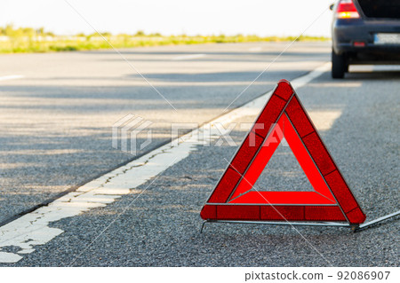 Red emergency stop sign (red triangle warning sign) and broken car on road 92086907