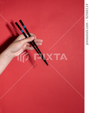 The hand holds chopsticks. Vertical frame on a bright red background. Copy of the space The hand holds chopsticks. Vertical frame on a bright red background. Copy of the space 92088114