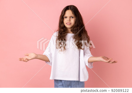 Portrait of annoyed frustrated little girl wearing white T-shirt standing with raised hands and indignant face asking why, annoyed by problem. Indoor studio shot isolated on pink background. Portrait of annoyed frustrated little girl wearing white T-shirt standing with raised hands and indignant face asking why, annoyed by problem. Indoor studio shot isolated on pink background. 92089122