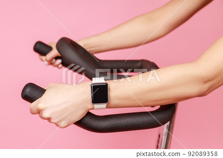 Closeup portrait of unknown woman hands with smartwatch on sport apparatus, sports equipment. Indoor studio shot isolated on pink background. Closeup portrait of unknown woman hands with smartwatch on sport apparatus, sports equipment. Indoor studio shot isolated on pink background. 92089358