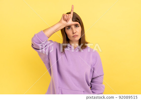 Portrait of upset disappointed young adult woman standing, showing looser gesture with hand on forehead, wearing purple hoodie. Indoor studio shot isolated on yellow background. Portrait of upset disappointed young adult woman standing, showing looser gesture with hand on forehead, wearing purple hoodie. Indoor studio shot isolated on yellow background. 92089515