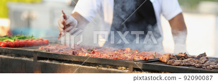 Professional male chef frying fresh meat on grill on open air 92090087