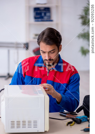 Young male repairman repairing oven at workshop Young male repairman repairing oven at workshop 92093286