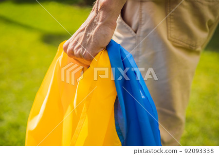 A man holds a Ukrainian flag in his hands. concept Ukrainian patriot, rally in support of Ukraine A man holds a Ukrainian flag in his hands. concept Ukrainian patriot, rally in support of Ukraine 92093338