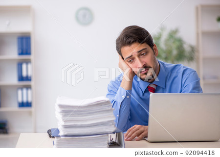 Young male employee unhappy with excessive work in the office Young male employee unhappy with excessive work in the office 92094418