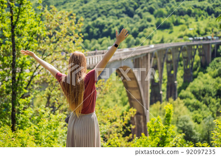 Montenegro. Woman tourist in background of Dzhurdzhevich Bridge Over The River Tara. Travel around Montenegro concept. Sights of Montenegro 92097235