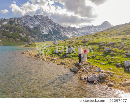 Family of tourists mom, dad and son in Mountain lake landscape on Durmitor mountain in Montenegro beautiful Durmitor National park with lake glacier and reflecting mountain Family of tourists mom, dad and son in Mountain lake landscape on Durmitor mountain in Montenegro beautiful Durmitor National park with lake glacier and reflecting mountain 92097477