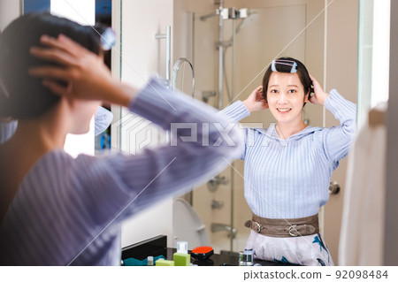 Young woman setting her hair in front of the mirror 92098484